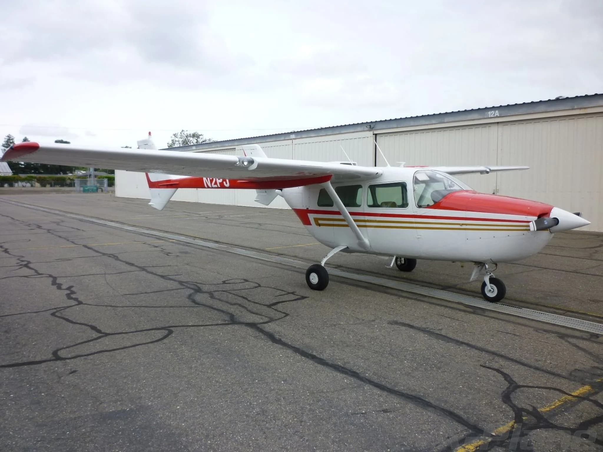 A white and red Cessna Skymaster N2PJ parked on an asphalt apron with hangars in the background.