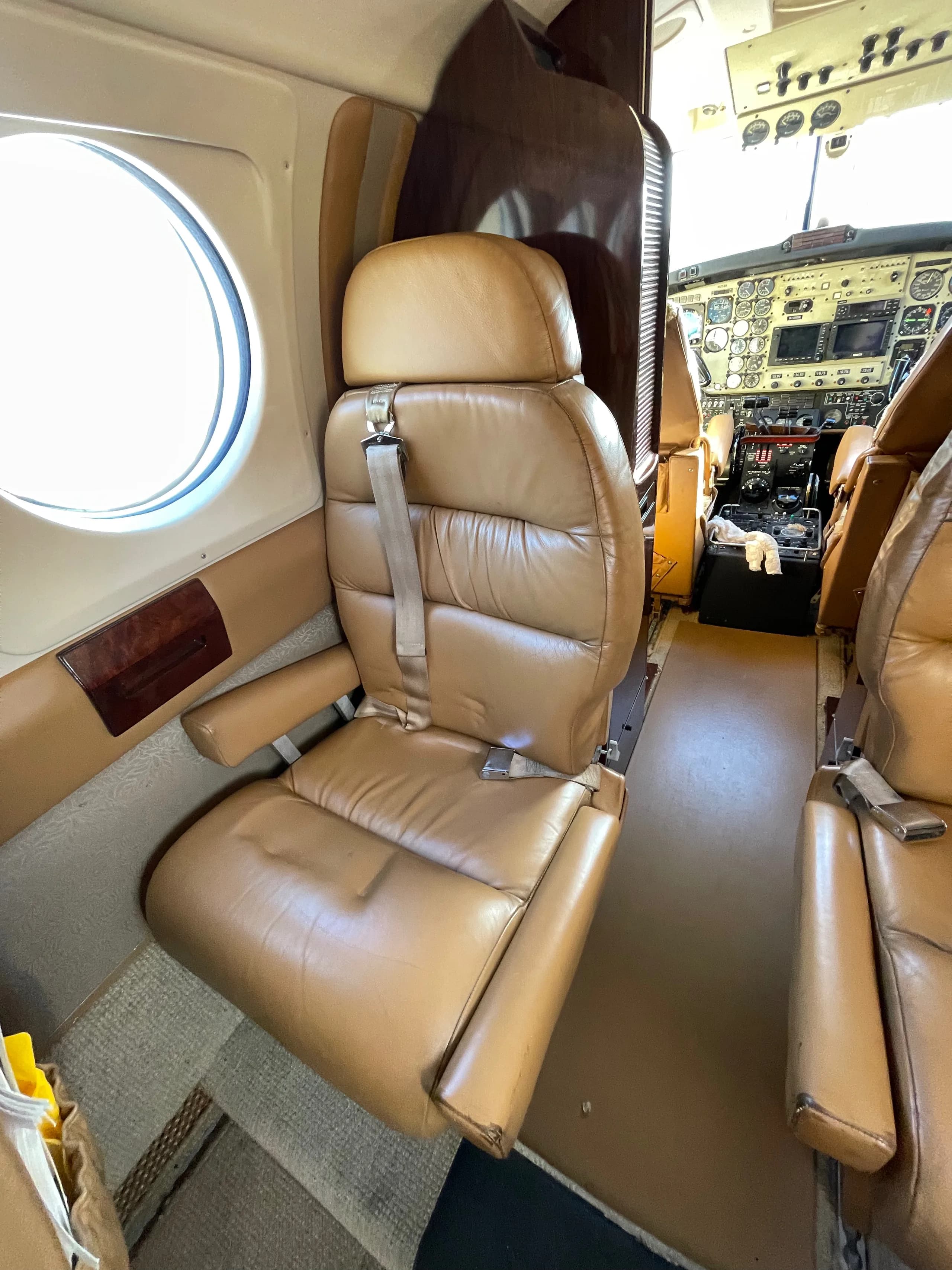 A tan leather passenger seat in the cabin of a private aircraft, with the cockpit visible in the background.