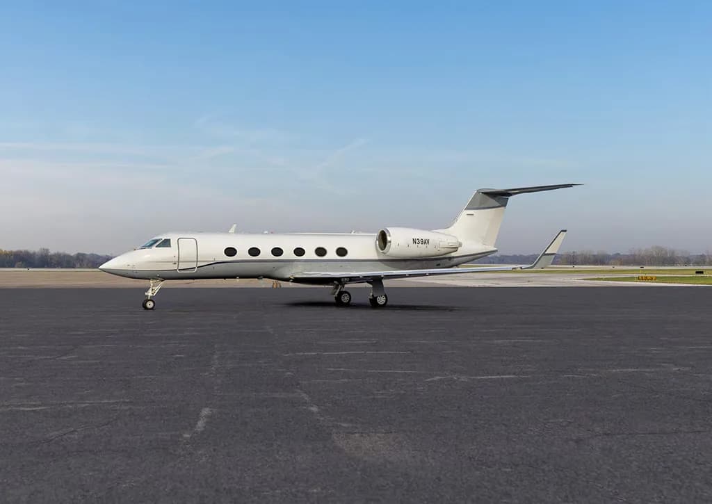 A white Gulfstream G550 aircraft (N39AV) is parked on a tarmac under a clear blue sky, viewed from the side.