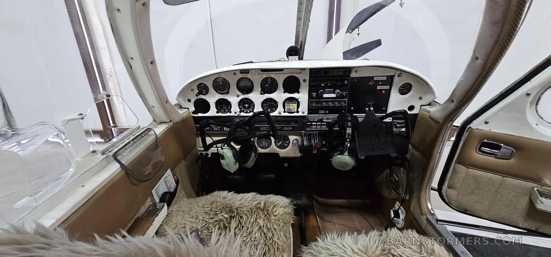The cockpit of a small aircraft with a white instrument panel, various gauges, and two headsets.