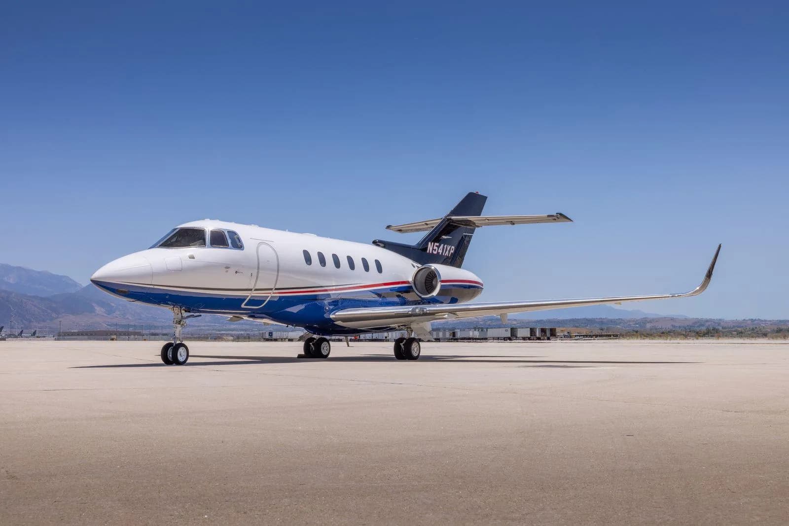 A Hawker 800XP business jet (N541XP) with blue and red stripes on an airfield under a clear sky.