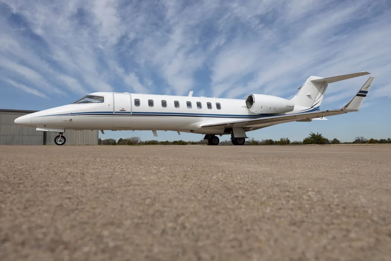A white aircraft with blue accents parked on the tarmac next to a building.