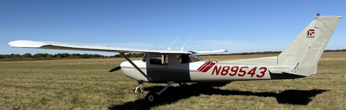 A Cessna 152 II aircraft with registration number N89543 parked on a grassy field, showing the side profile.