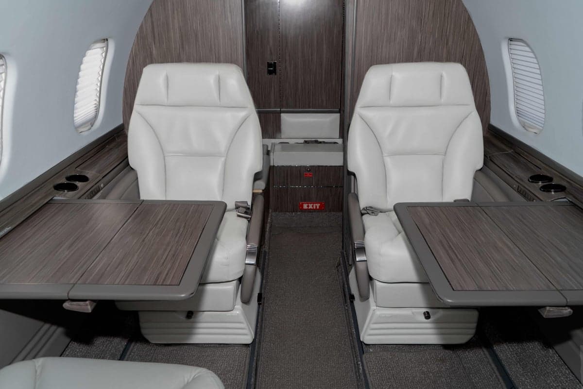 Two white leather seats with wooden tables in the aircraft cabin.