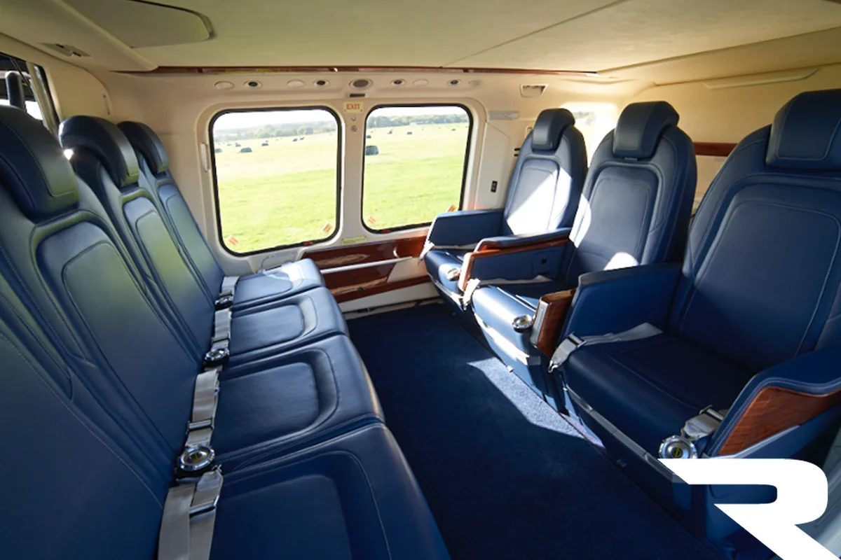 Interior view of a helicopter cabin with blue leather seats, looking out at a green field.