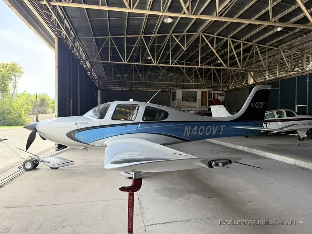 A three-quarter front view of a white and blue Cirrus SR22 aircraft, registration N400VT, parked in a hangar.