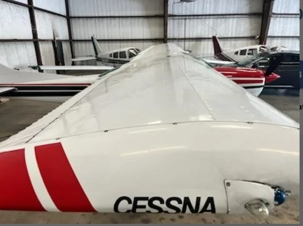 Top-down view of the white wing of a Cessna 182 Skylane with red stripes, inside a hangar.