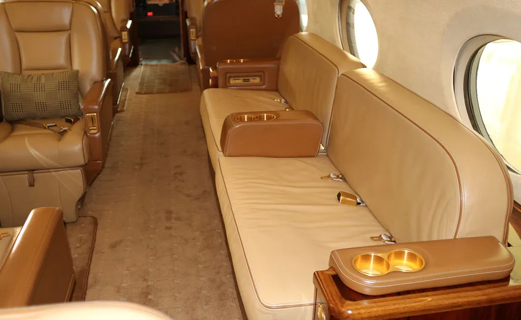 A tan leather sofa with cup holders in the luxurious interior of a private jet.
