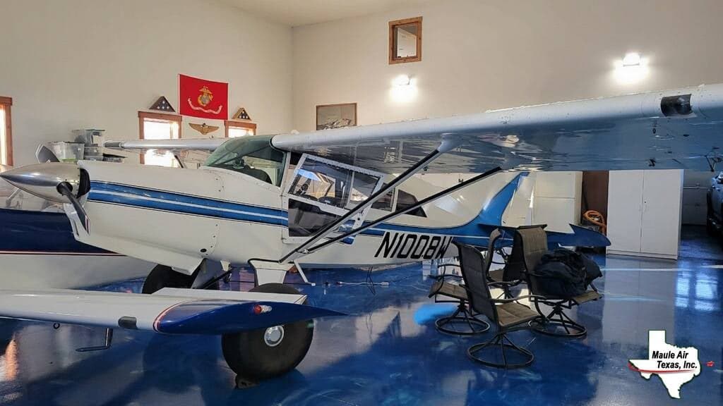 A white and blue Maule aircraft, N1008W, parked inside a hangar with a blue floor.