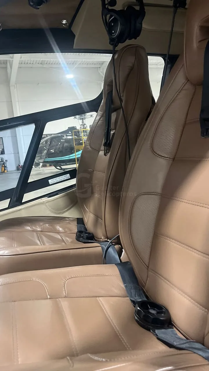 The interior of a helicopter features brown leather seats and a view of another aircraft outside.