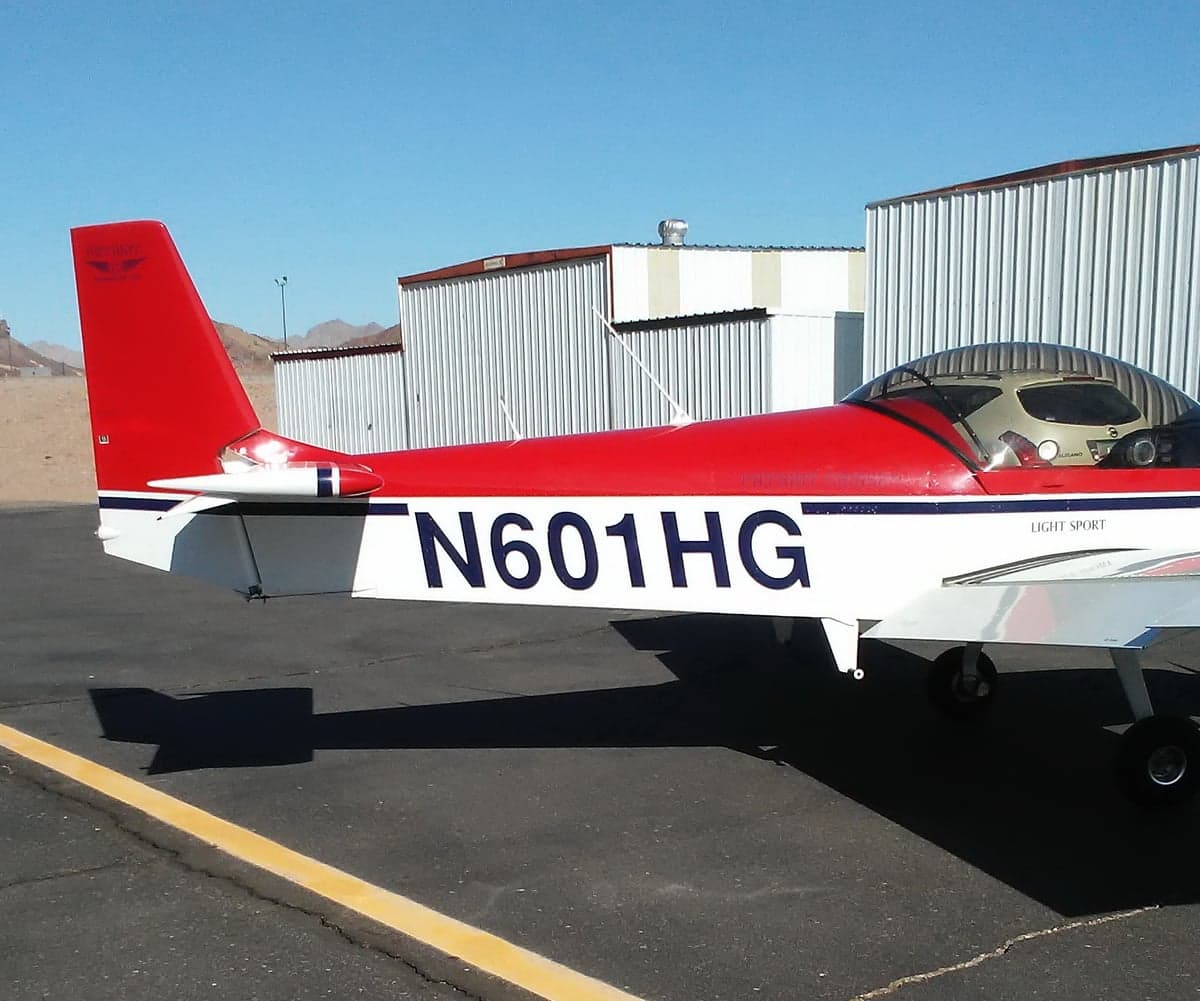 A close-up view of the red and white tail and fuselage of light sport aircraft N601HG, parked on an airfield.