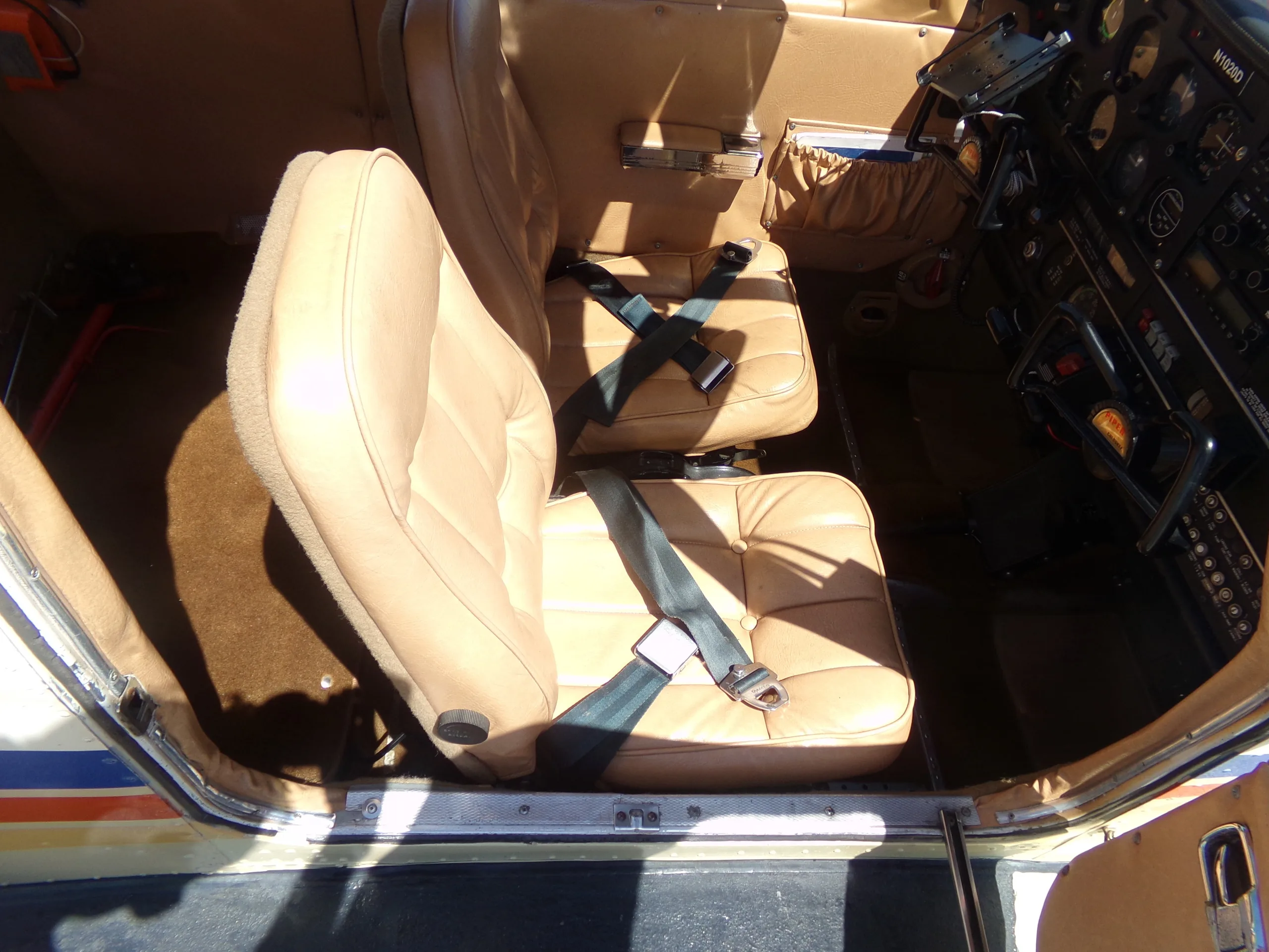 The tan leather front seats of a small aircraft cabin, with seatbelts fastened.
