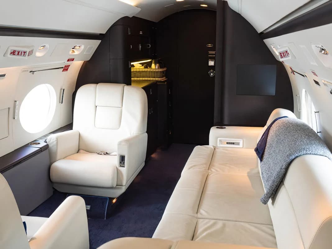 View of the aircraft interior with white leather seats and dark wood accents.