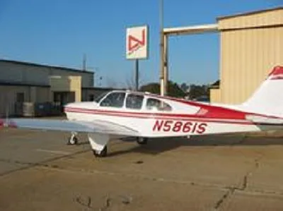A white and red Beechcraft Bonanza N5861S parked on an asphalt ramp with hangars and a sign in the background.