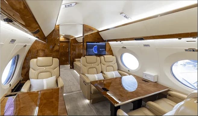 The luxurious interior cabin of a private jet with beige seats, a dining table, and wood paneling.