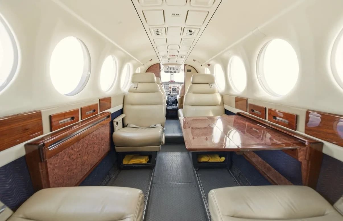 The aircraft's cabin interior features beige leather seating, wood paneling, and a central table.
