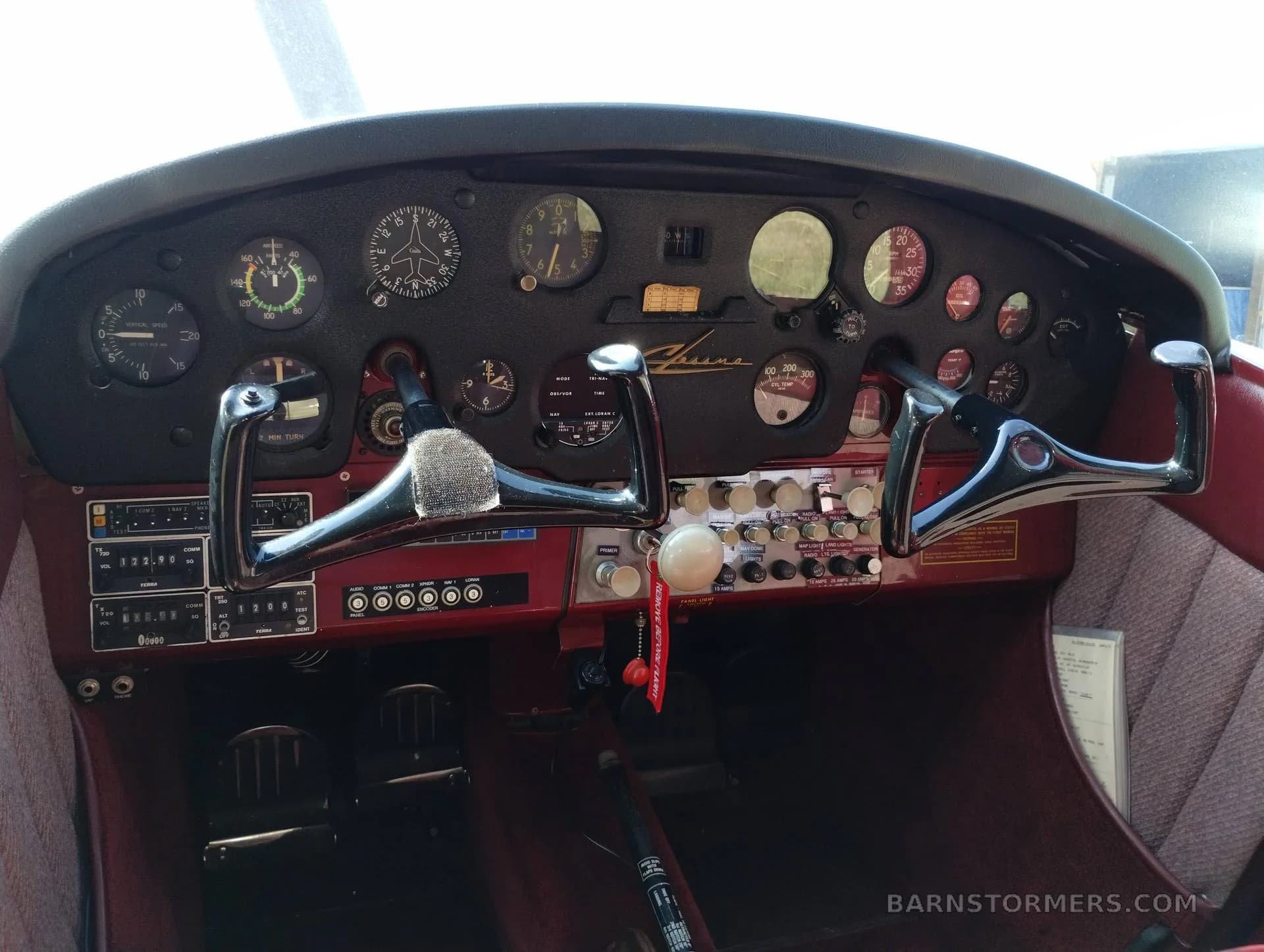 The cockpit of a small aircraft shows the instrument panel with various gauges and two control yokes.