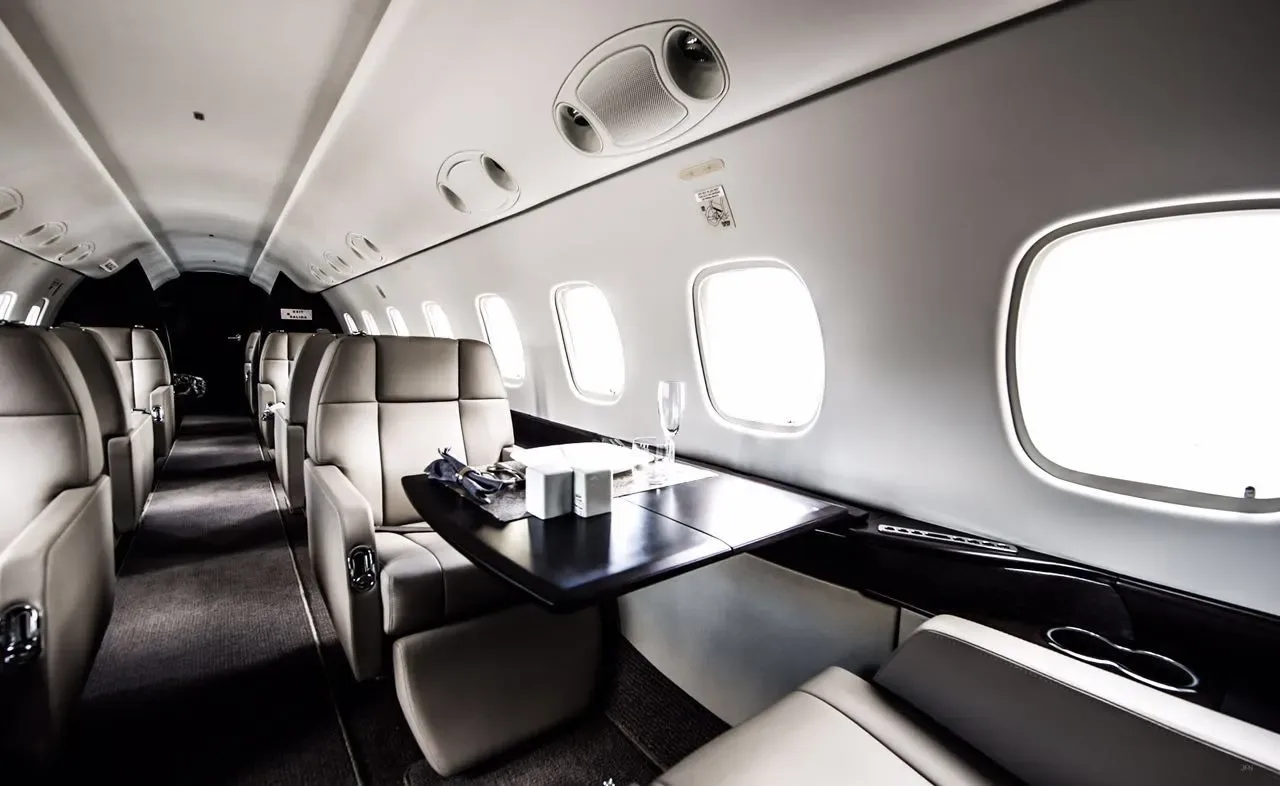 A view inside a private jet cabin showing beige leather seats, large windows, and a table set for dining.