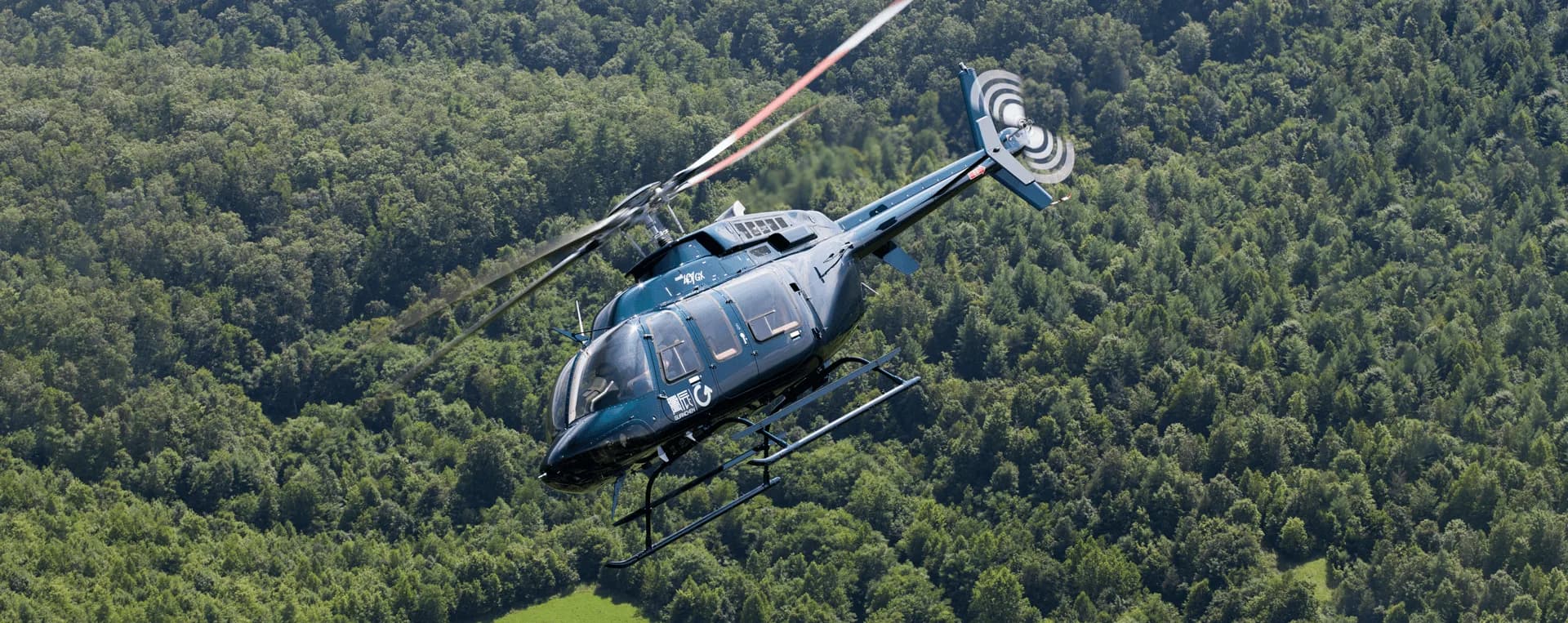Dark blue helicopter flying over a forest.