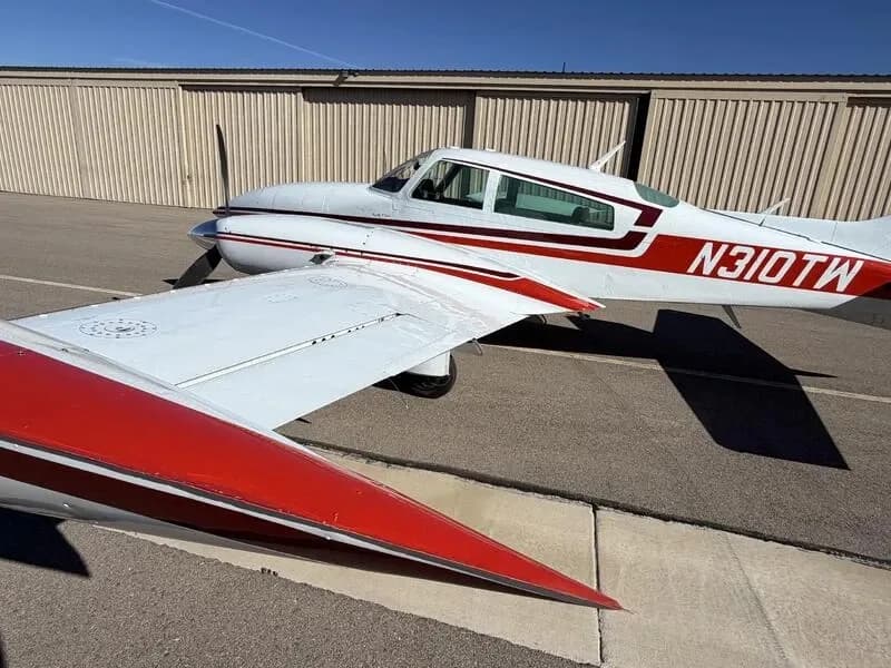 Close-up view of the wing, tip tank, and fuselage of a white and red Cessna 310 aircraft.