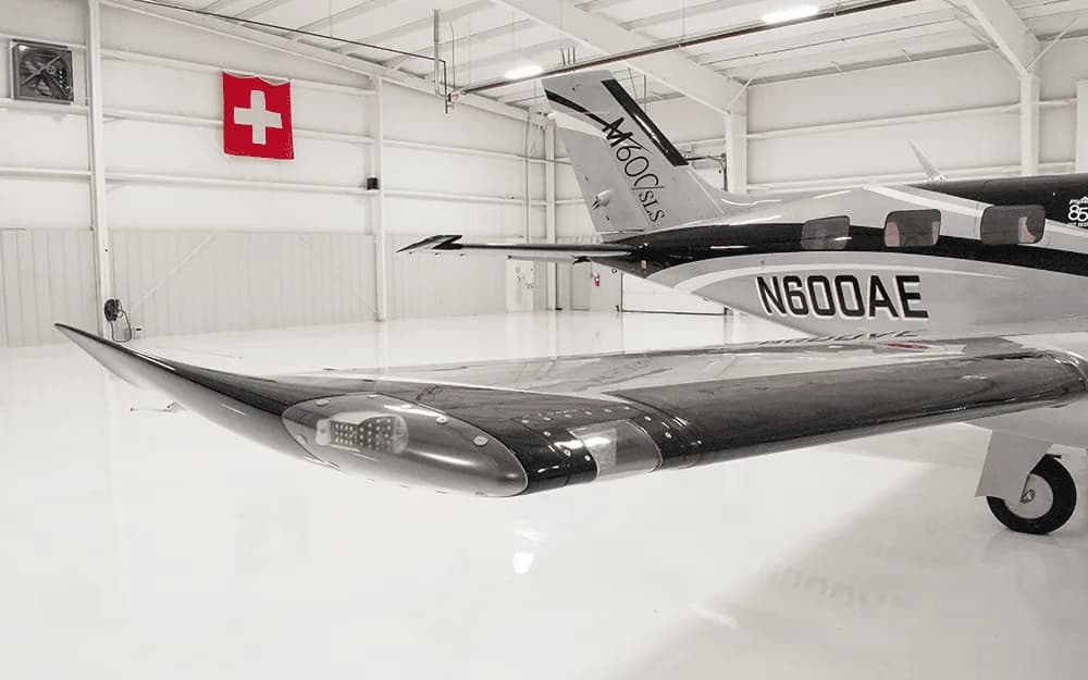 A close-up view of the wingtip and tail of the Piper M600/SLS aircraft (N600AE) in a hangar, showing its black and silver livery.