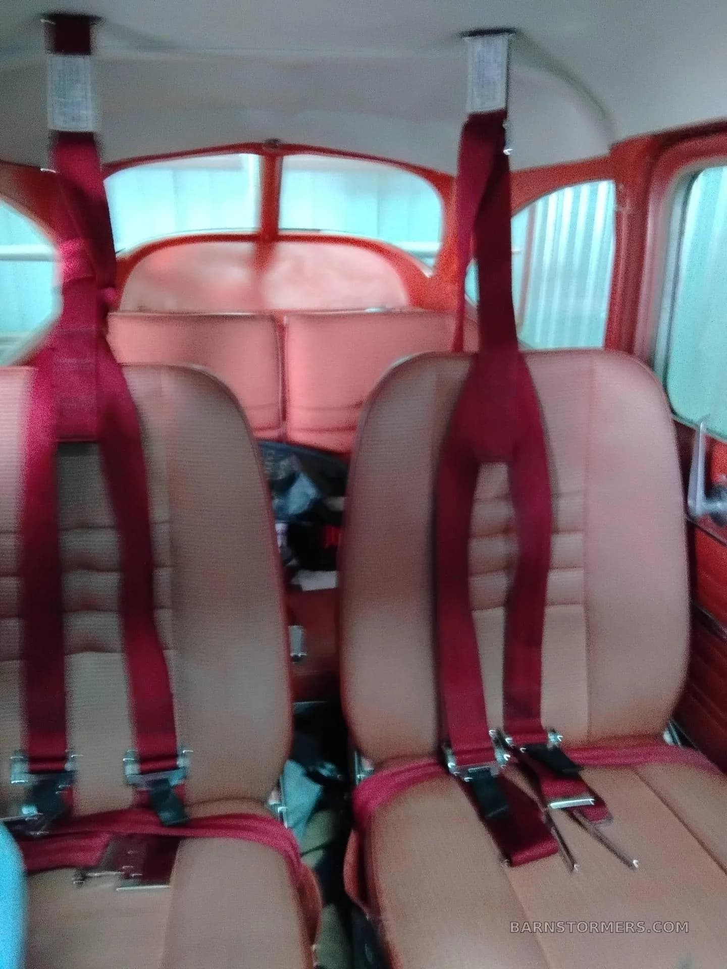 The two rear seats of a small aircraft cabin, featuring red seatbelts.