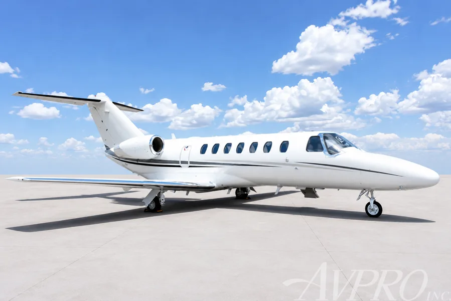 A white Cessna Citation jet with black and grey stripes parked on an airfield, viewed from the front-right side.