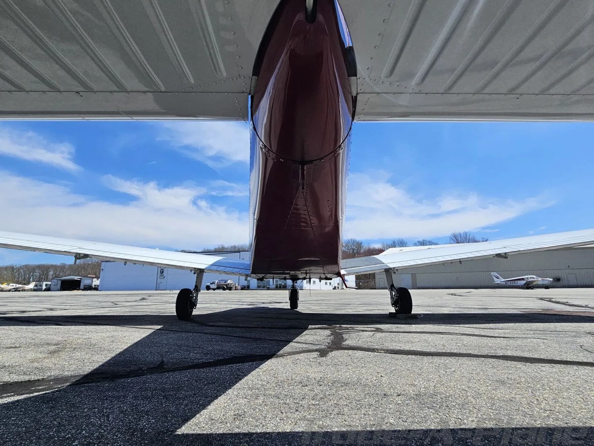 Low-angle view from under the tail of a white and maroon Piper PA-28 aircraft on an airfield.