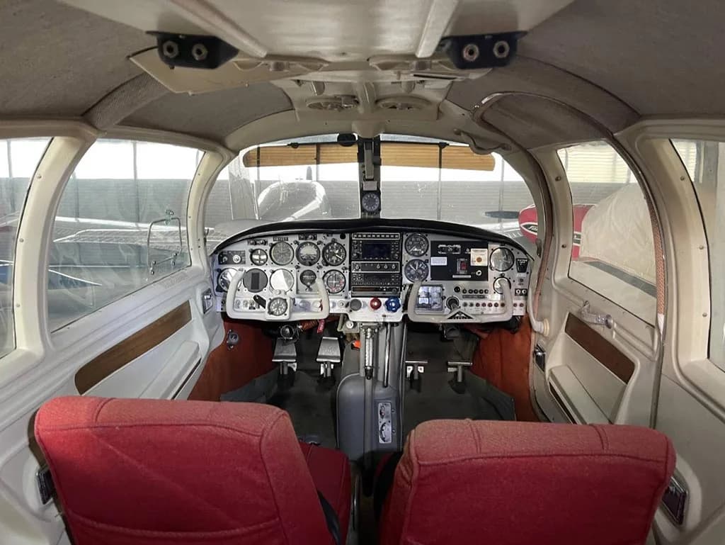 The cockpit of a small aircraft, viewed from the rear seats, showing the instrument panel and dual controls.