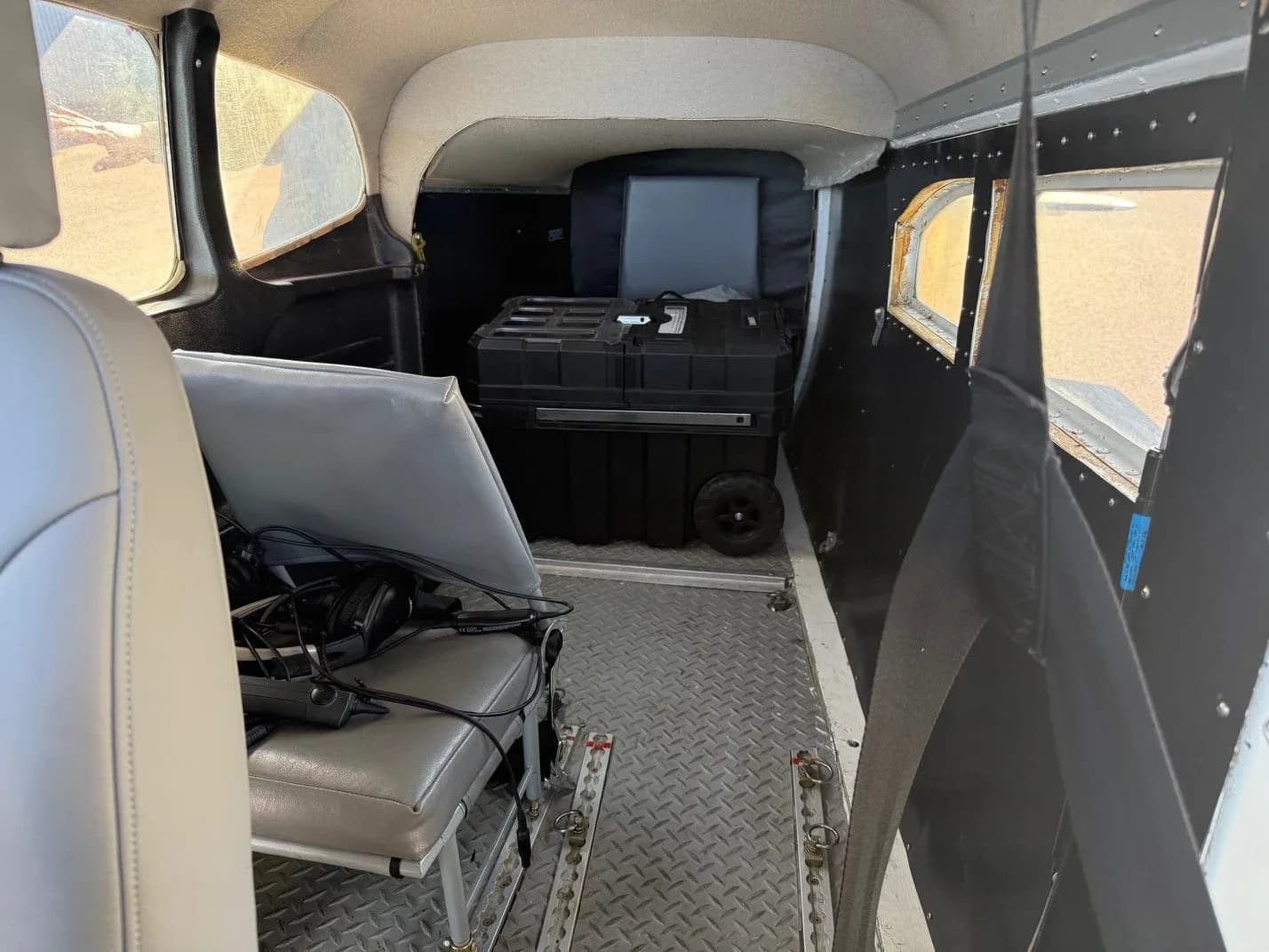 Interior view of an aircraft cabin with grey seats and a black cargo box.