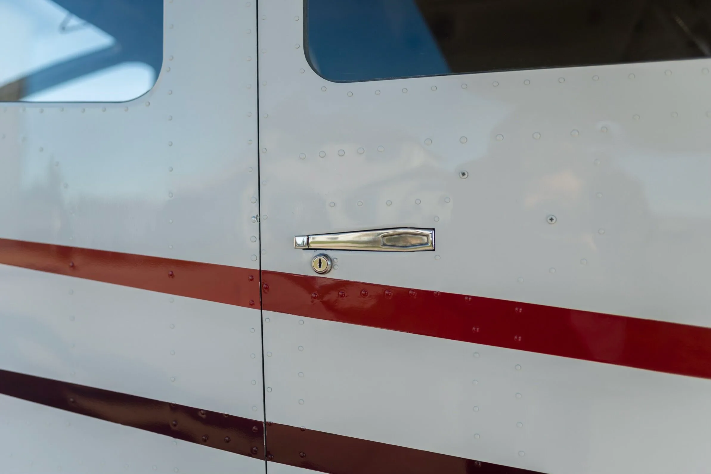 A close-up of the aircraft's white fuselage, showing a silver door handle and red and dark red stripes.