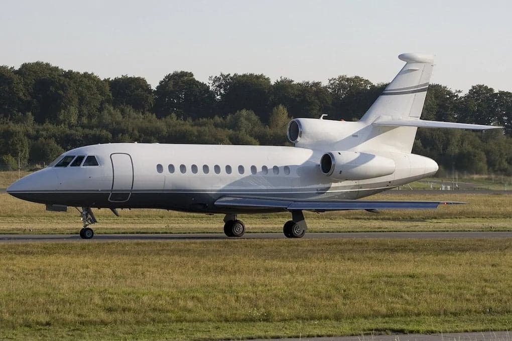 Side view of a white and gray Falcon jet on the ground.