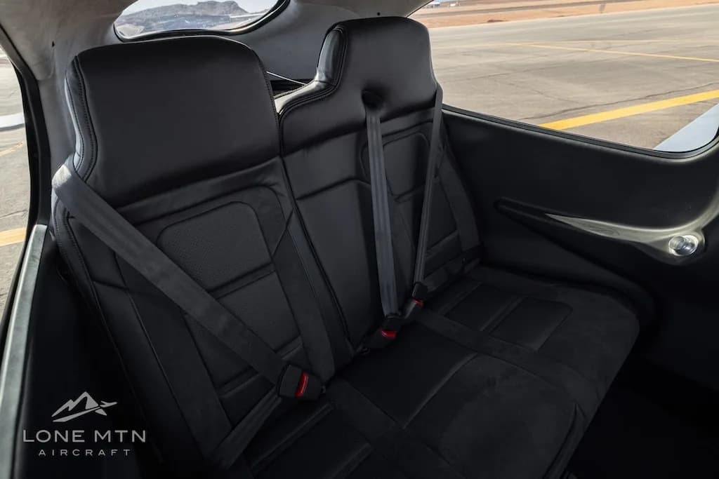 The black leather rear seats of the aircraft cabin with seatbelts, viewed from the side.