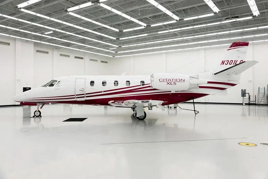A white Cessna Citation XLS private jet with a maroon stripe and registration N301LG is parked in a brightly lit hangar, viewed from the rear-left.