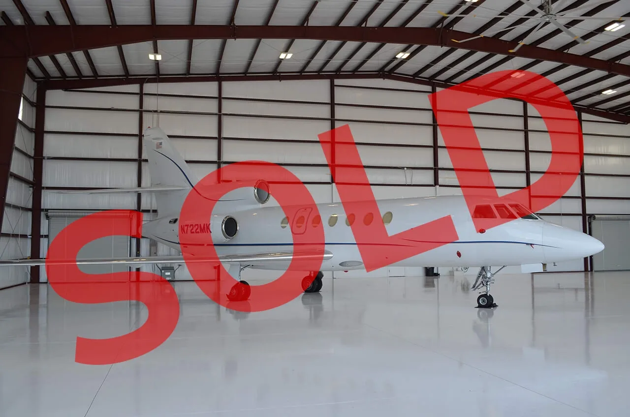 A white business jet with a blue stripe is parked inside a hangar, viewed from the side.