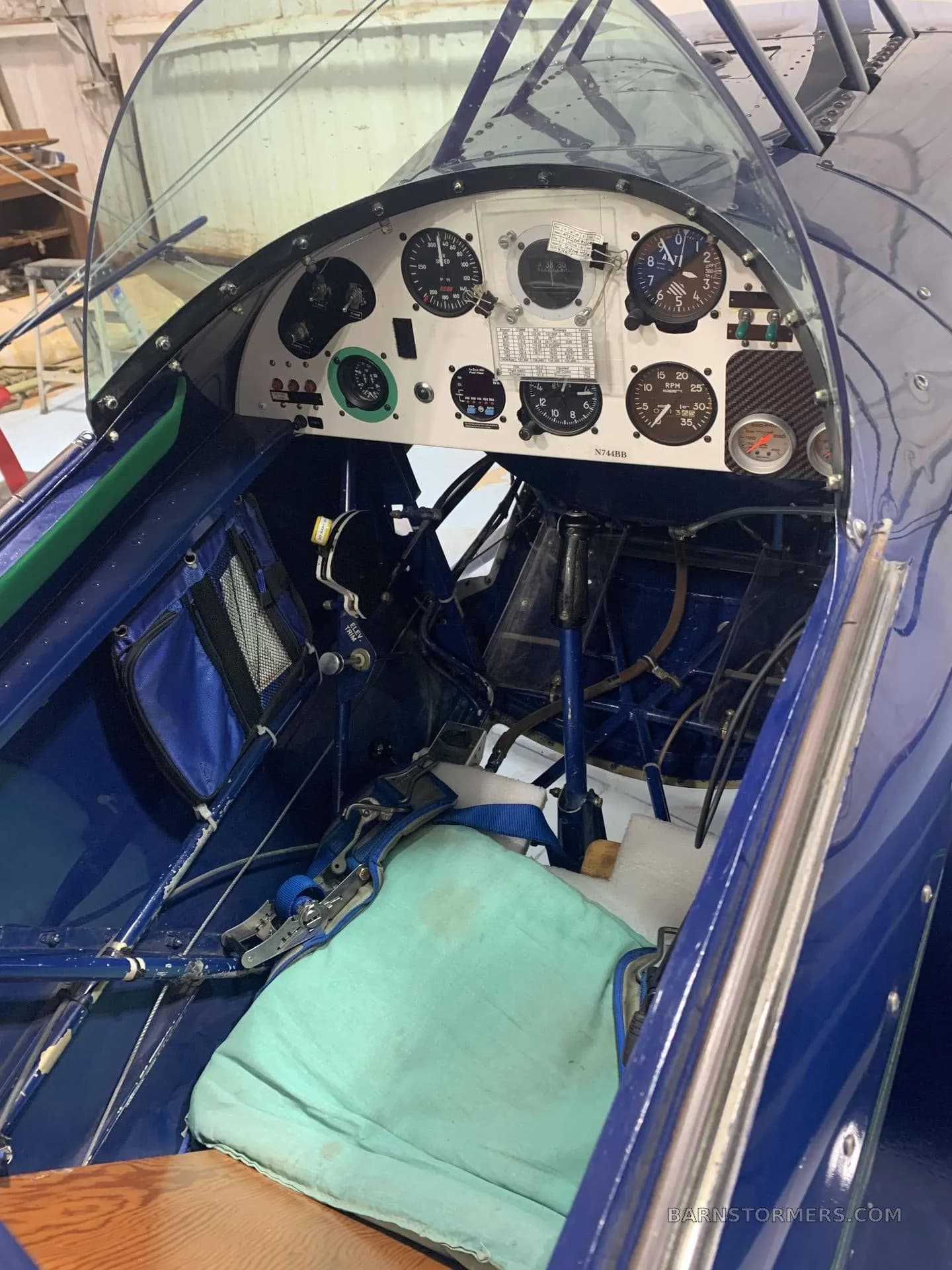 The cockpit of a blue Pitts S1-S biplane, showing the instrument panel and a light blue seat cushion.