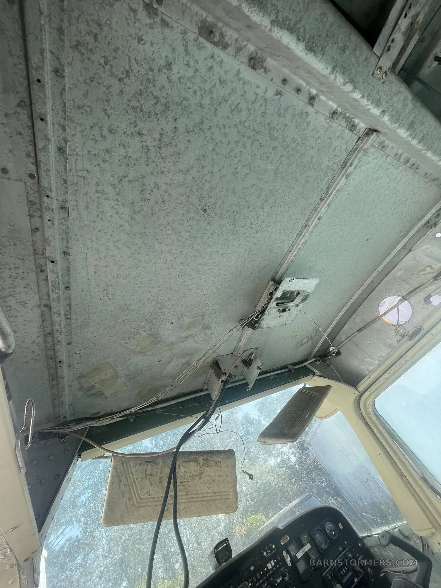 The weathered and stripped ceiling of a light aircraft cabin, showing exposed structural elements and wiring.