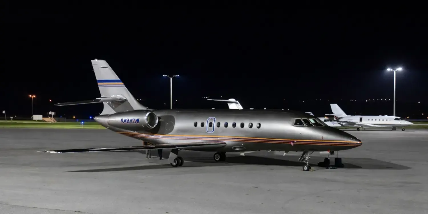 Side view of a Falcon aircraft with a silver and orange paint scheme on the tarmac at night.