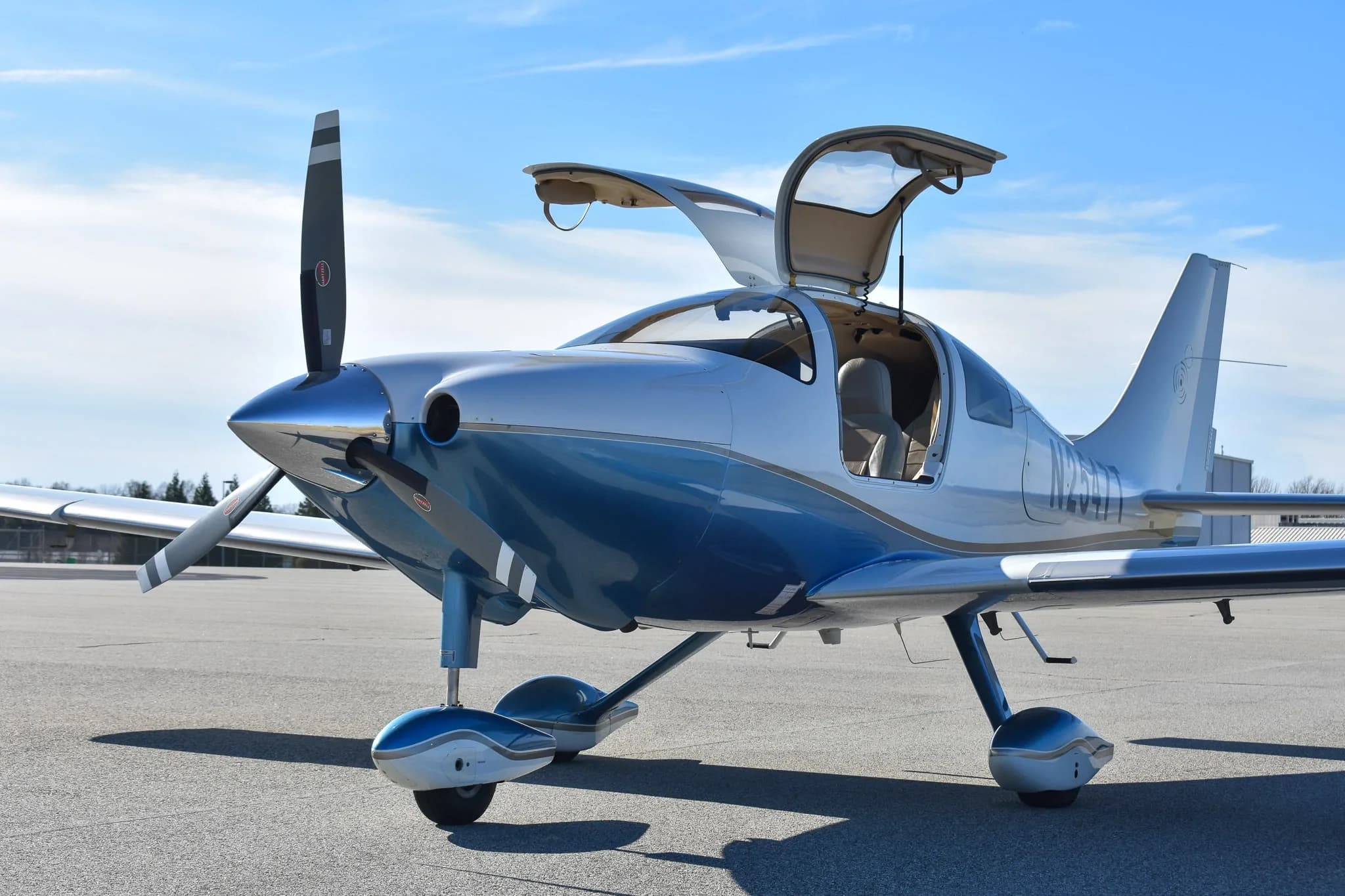 A front-side view of the white and blue single-engine aircraft, N2547T, with its gull-wing doors open on an airfield.