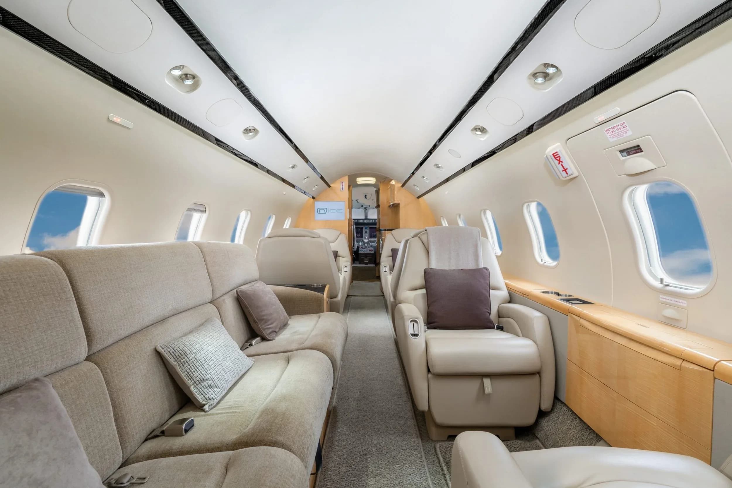 The interior of a private jet cabin with a beige fabric sofa on the left and a beige leather seat on the right, looking towards the rear.