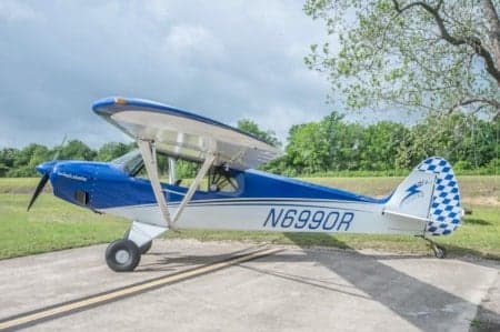A blue and white Piper Cub sits on the tarmac.