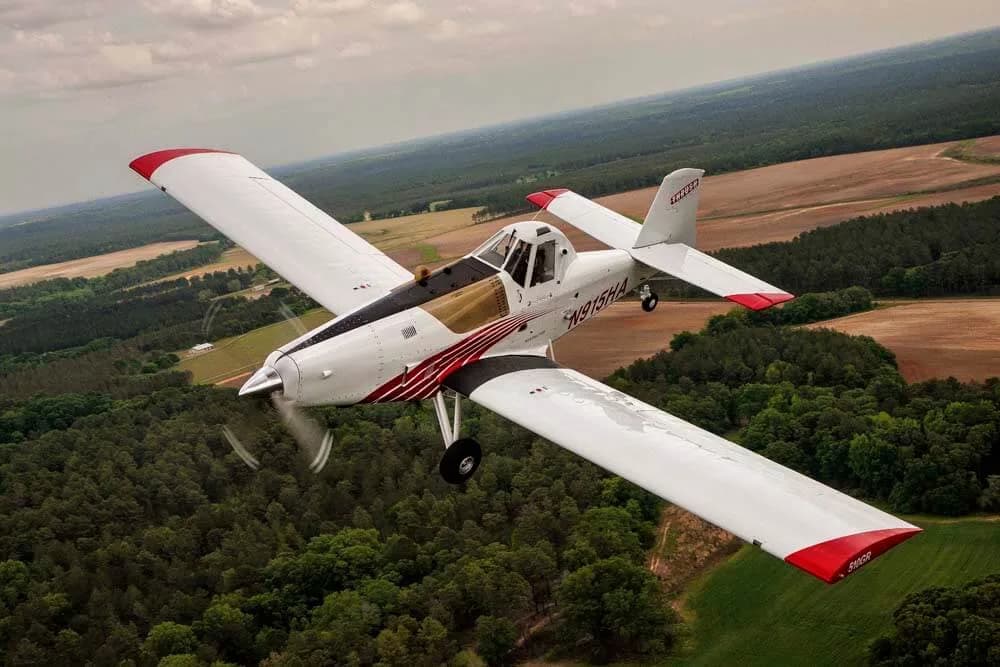 Aerial view of a white and red Air Tractor crop duster flying over trees.