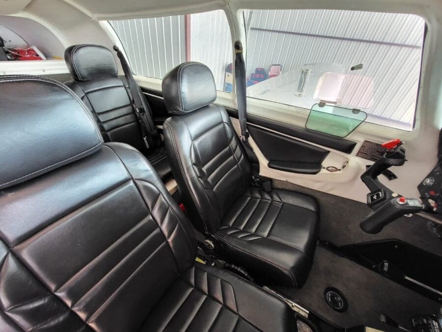 The black leather seats of a Mooney M20J aircraft cabin, viewed from the rear.