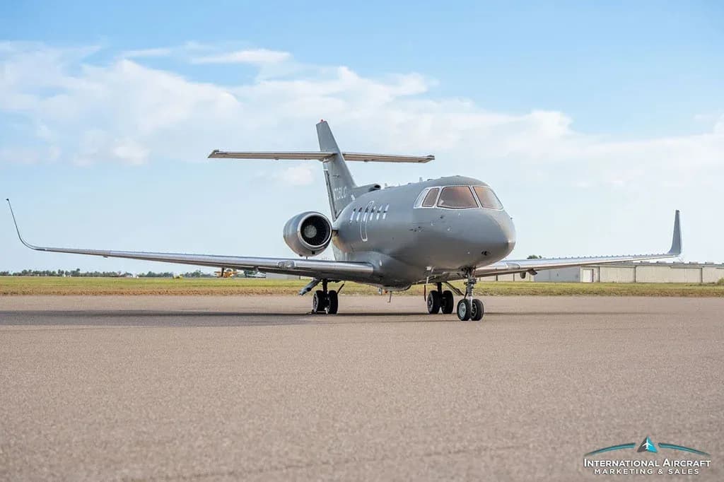 A gray business jet, N726LC, is viewed from the front on an asphalt runway under a blue sky.