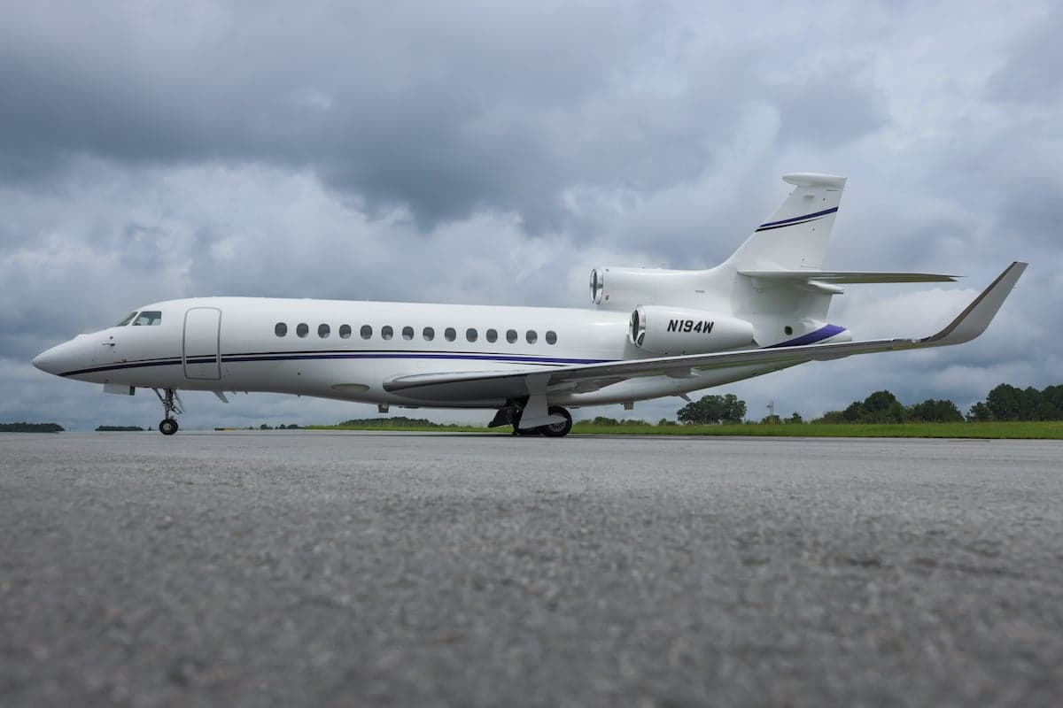 A Falcon 7X aircraft with registration N194W is parked on the tarmac under a cloudy sky.