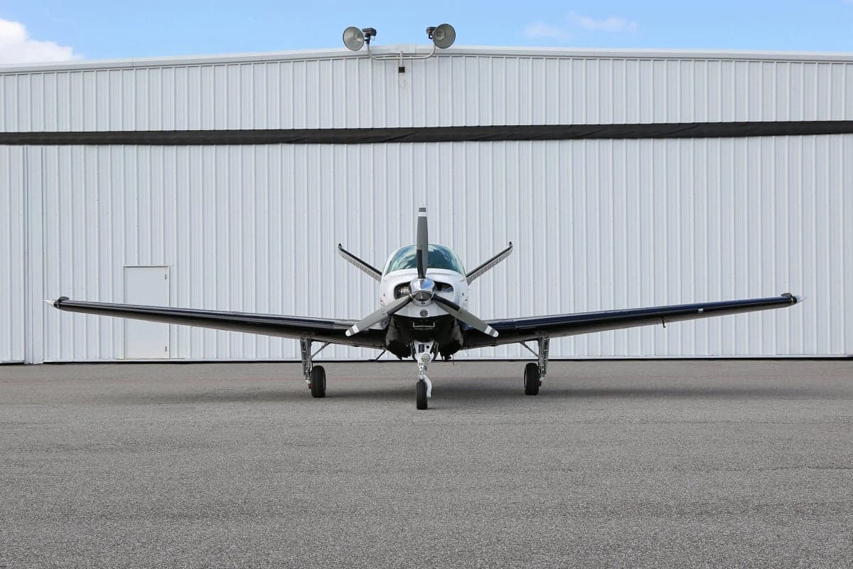 Front view of a Beechcraft Bonanza aircraft on the ground in front of a hangar.