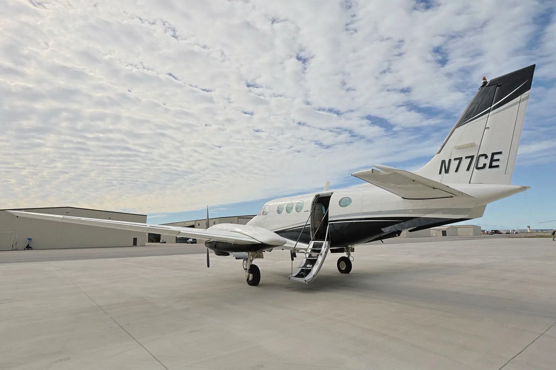 A rear-left quarter view of the N77CE twin-engine turboprop aircraft with its passenger door open.