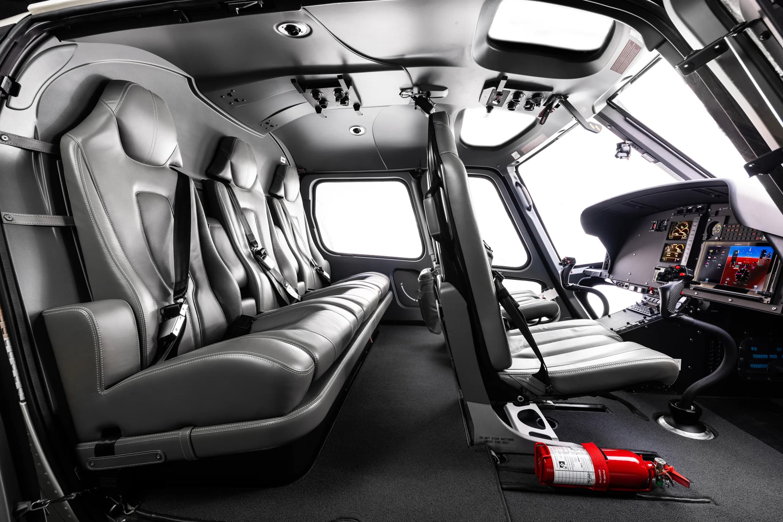 The grey leather interior cabin of a helicopter with seats and a partial view of the cockpit.