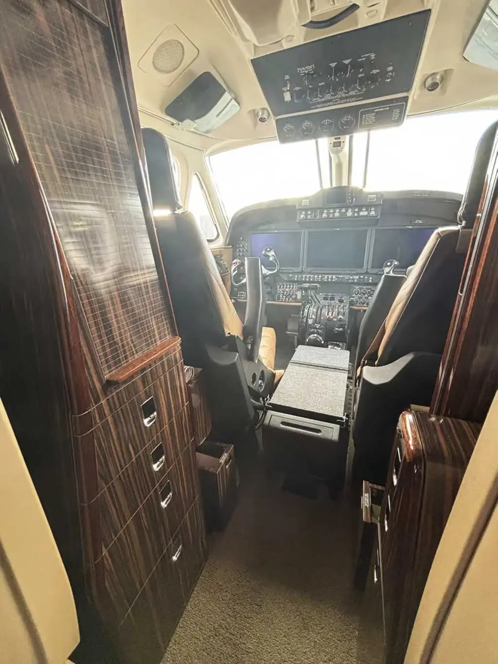 View into the aircraft cockpit from the cabin, showing the instrument panel and pilot seats.