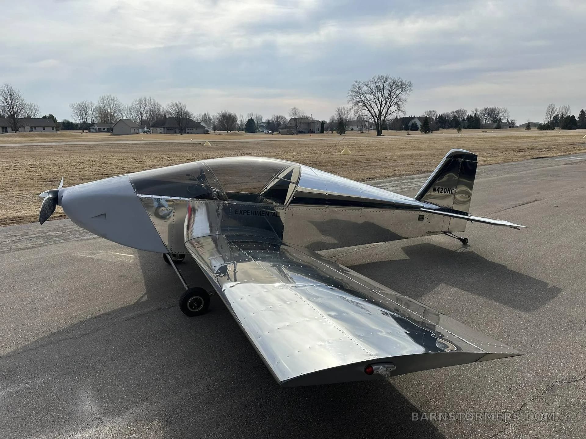 A shiny silver and black experimental aircraft with "N420HC" on the tail, parked on an asphalt taxiway.